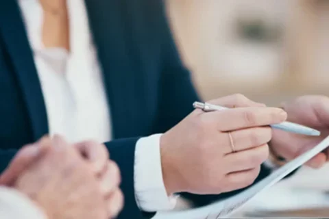 A hand holds a pen in one hand and a blank sheet of paper in the other, preparing to begin writing
