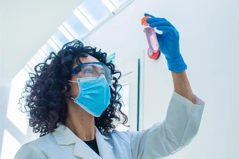 Woman in surgical mask and lab goggles holding up lab tube