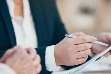 A hand holds a pen in one hand and a blank sheet of paper in the other, preparing to begin writing