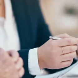 A hand holds a pen in one hand and a blank sheet of paper in the other, preparing to begin writing